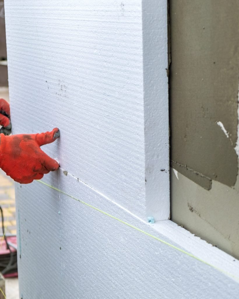 Construction worker installing styrofoam insulation sheets on house facade wall for thermal protection.
